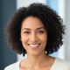 Smiling woman with dark, curly hair and warm brown eyes, exuding confidence and satisfaction. Softly blurred slate blue and b